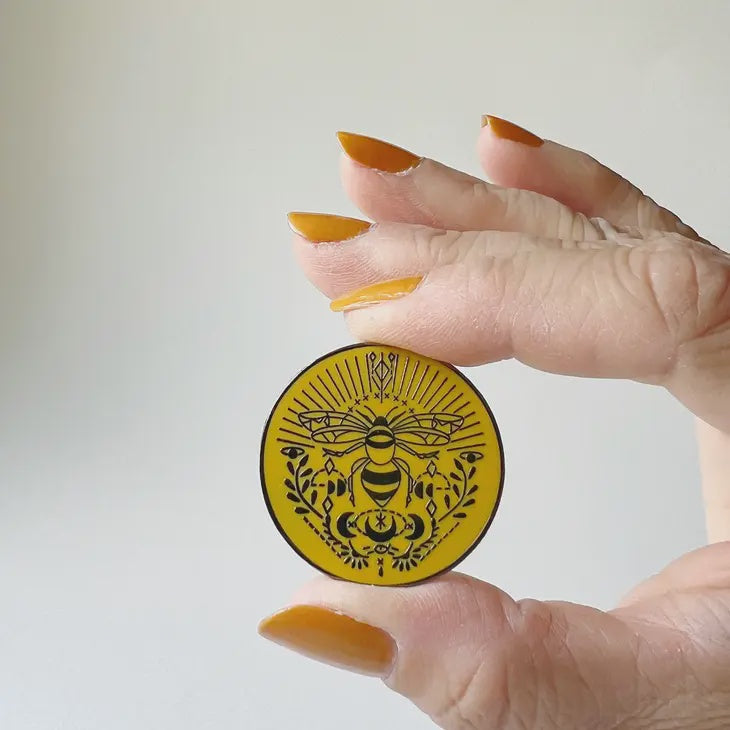 Yellow enamel needle minder with bee and scroll design around it.